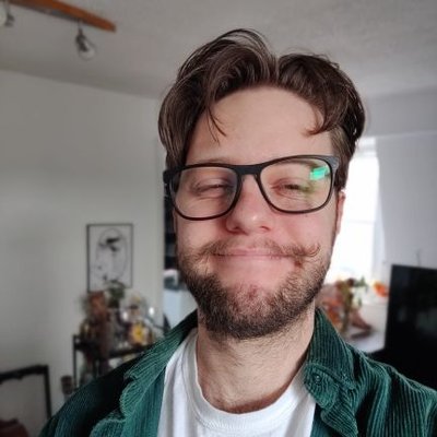 a profile photograph of Luke. He is wearing glasses, has a twirly moustasche and a big smile.