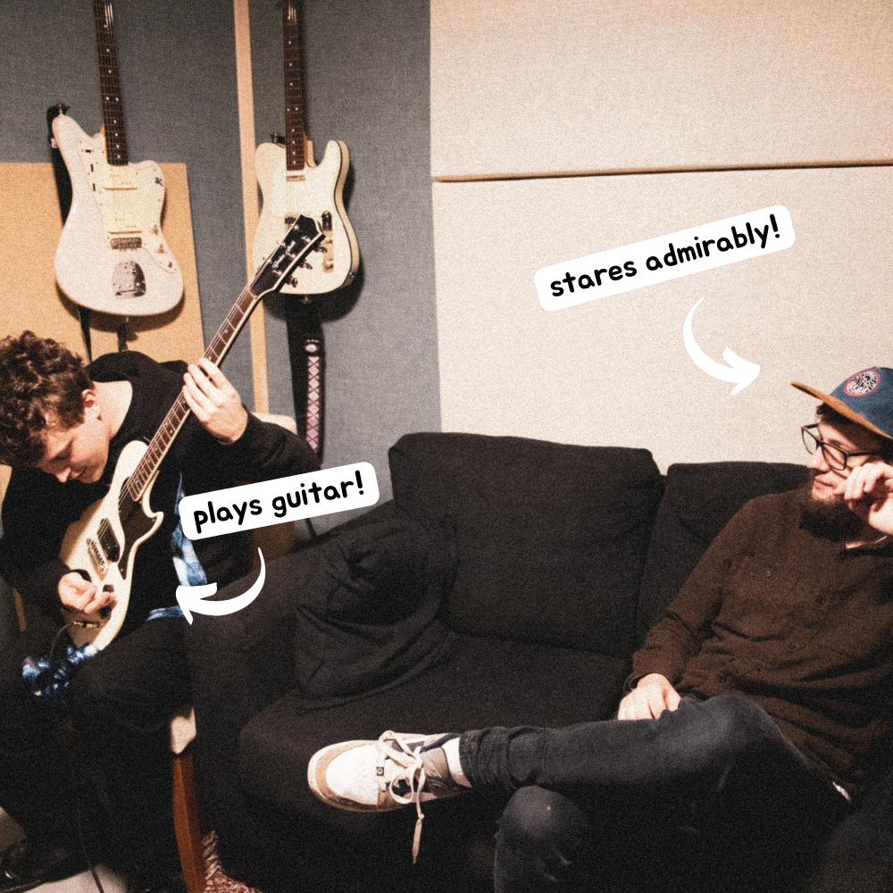 Luke and Corey from Scrub sat in a recording studio. Corey is playing a guitar. Text popouts are on the image. #1 points to Corey and says 'plays guitar!'. #2 points to Luke and says 'stares admirably!'